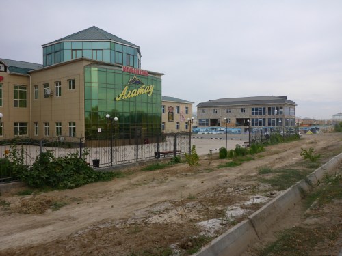 Kyzylorda Abai Avenue - but could be any town, some new flash building with grand entrance that cannot be used and dirt road approach with unfinished building next door, all boarded up.